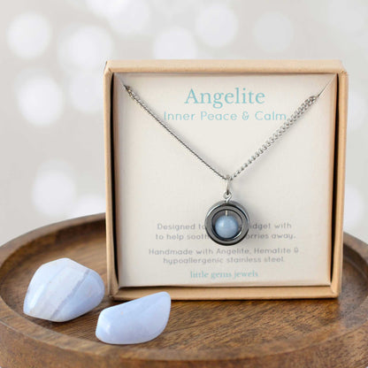 Necklace with pendant and stones in a box labeled 'Angelite' on a wooden surface.