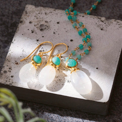 Gold earrings with turquoise stones on a white stone surface