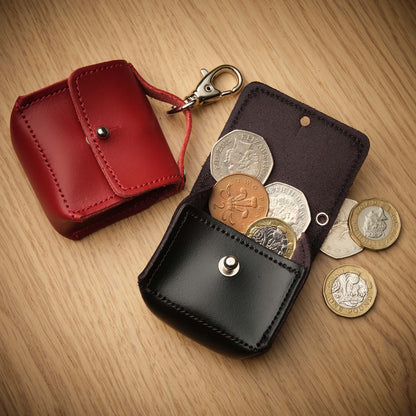 Black leather coin pouch with coins on a wooden surface, next to a red one.