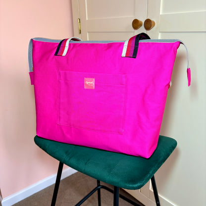 Berry Riot bright pink shoulder tote with striped handles and a front pocket, angled front view on a green velvet stool