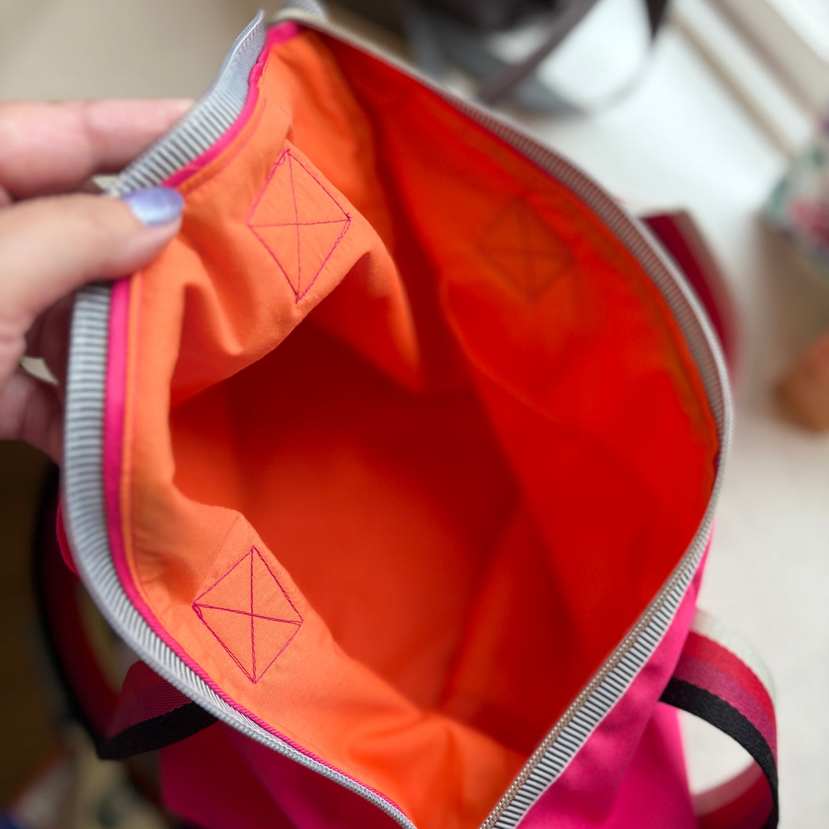 Inside of the Berry Riot shoulder tote showing the bright tangerine orange cotton lining with stitched corner details and a striped zip