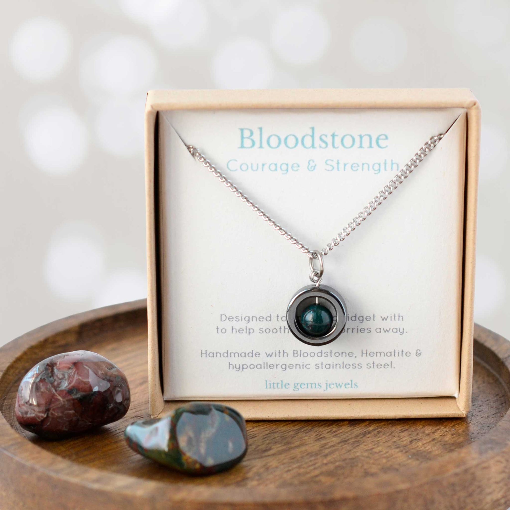 Necklace with pendant in a box labeled 'Bloodstone: Courage & Strength' on a wooden surface.