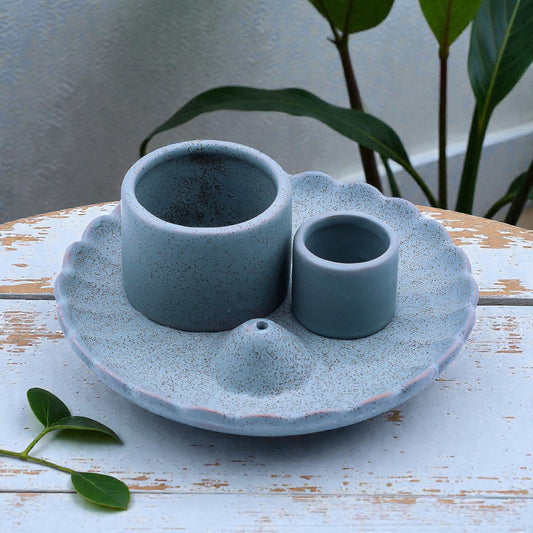 Blue ceramic incense and smudge stick holder set on a wooden surface with plants in the background