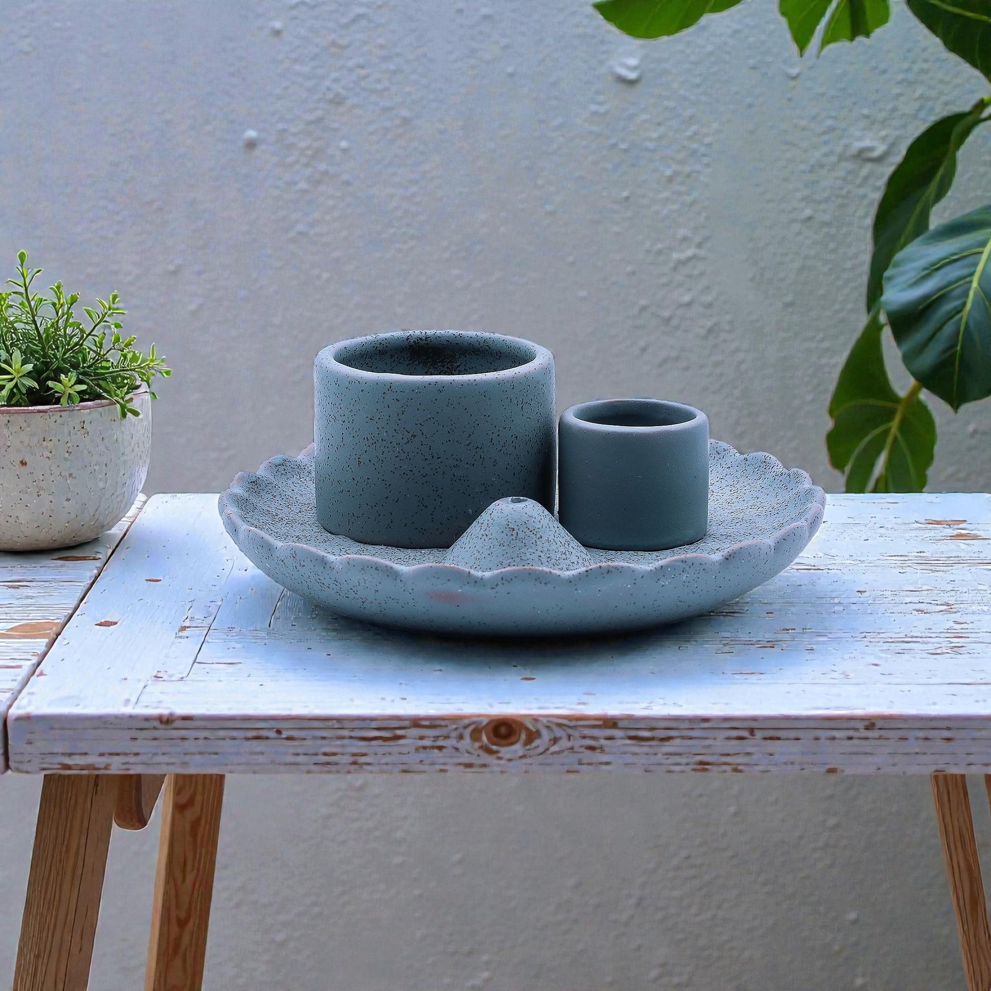 A blue ceramic incense and smudge stick holder on a wooden table with plants in the background.