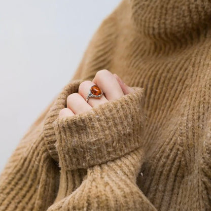 Close-up of a hand wearing a ring with a brown stone, holding a brown knitted sweater sleeve.