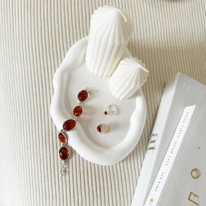 Jewelry set with amber stones on a white dish with seashells, next to a book on a textured surface.