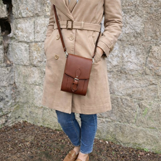 Person wearing a beige coat with a brown leather bag against a stone wall.
