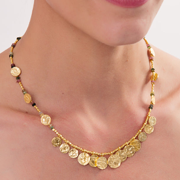 Gold necklace with circular pendants on a person against a neutral background