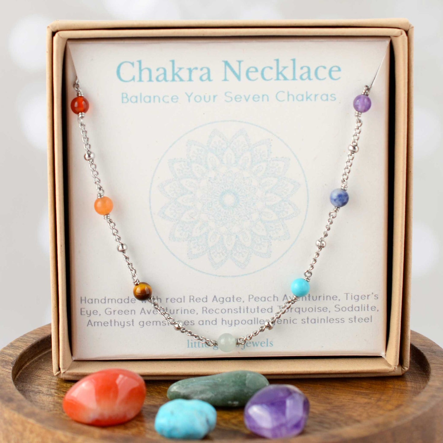 Chakra necklace with colorful beads on a branded card, displayed on a wooden surface.