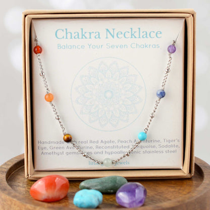 Chakra necklace with colorful beads on a branded card, displayed on a wooden surface.
