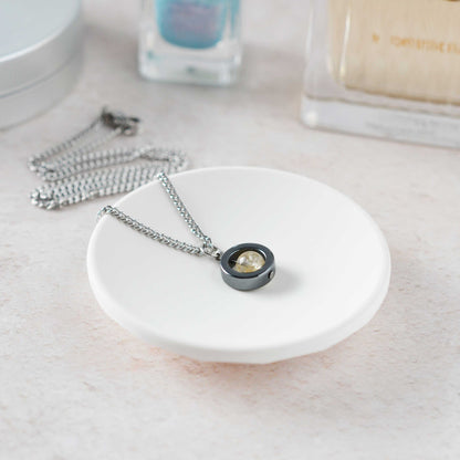 Necklace with a pendant on a white dish, with nail polish and a bottle in the background.