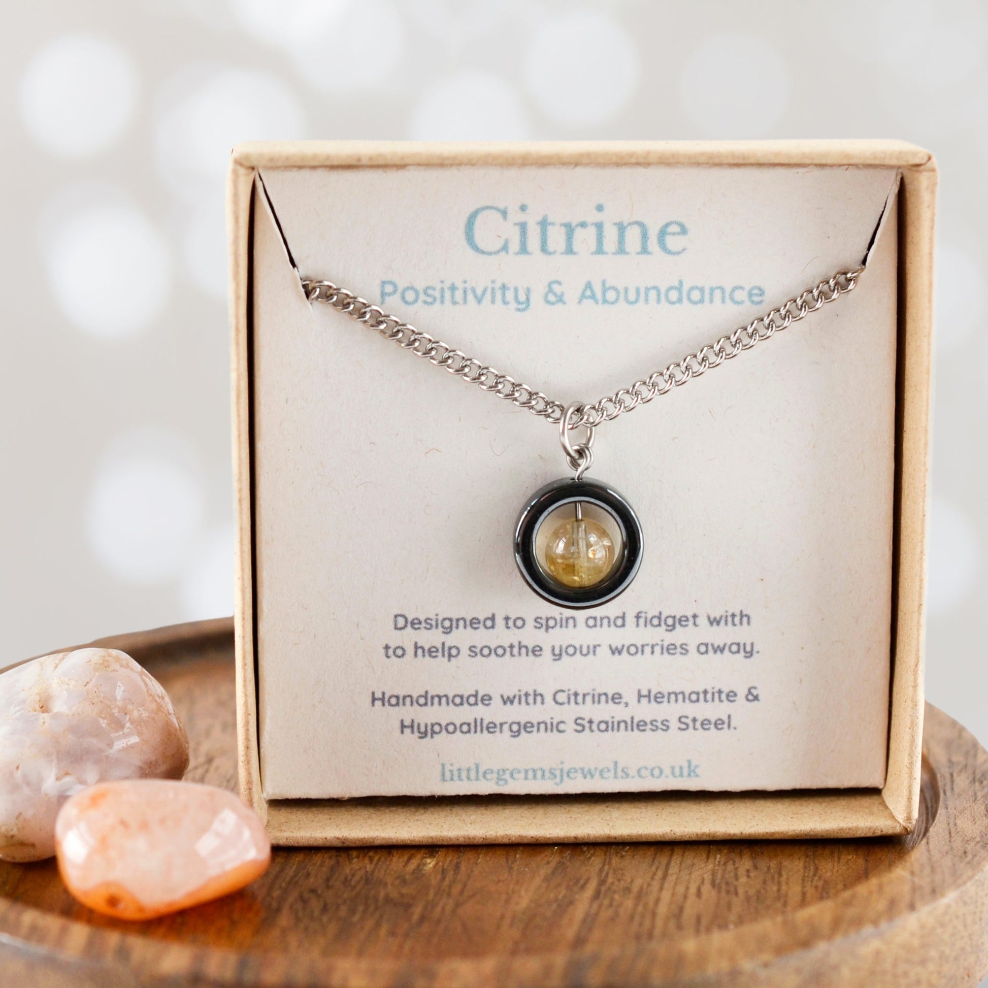 Citrine necklace in a box with card detailing properties and materials, on a wooden surface.