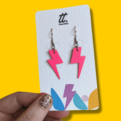 Pink lightning bolt earrings on a branded card against a yellow background