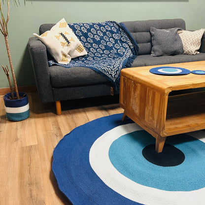 Cotton Rope Evil Eye Rug in a living room, under a wooden coffee table in front of a grey sofa with blue and white cushions