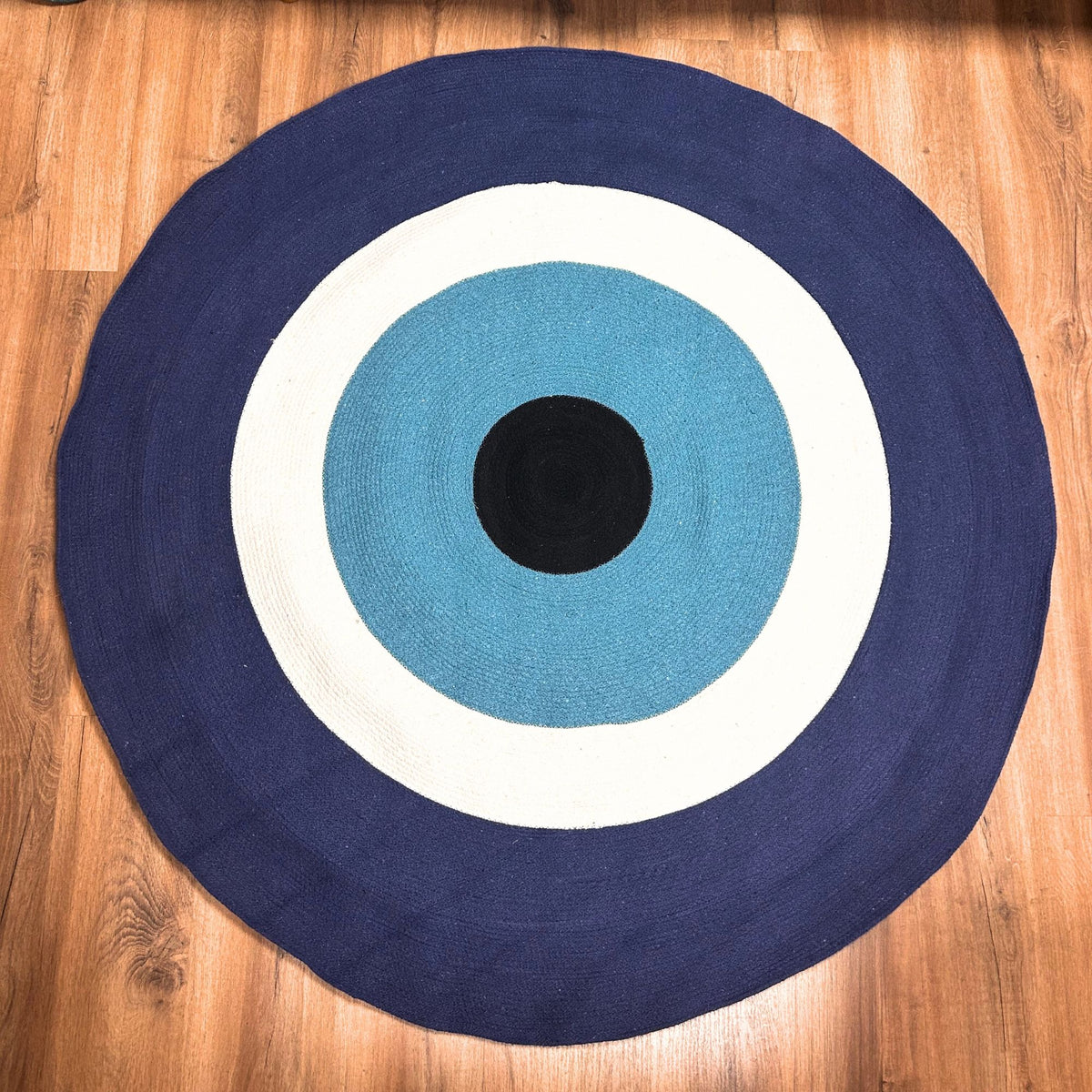 Round Cotton Rope Evil Eye Rug on a wooden floor, with a navy outer ring and white, turquoise and black rings inside