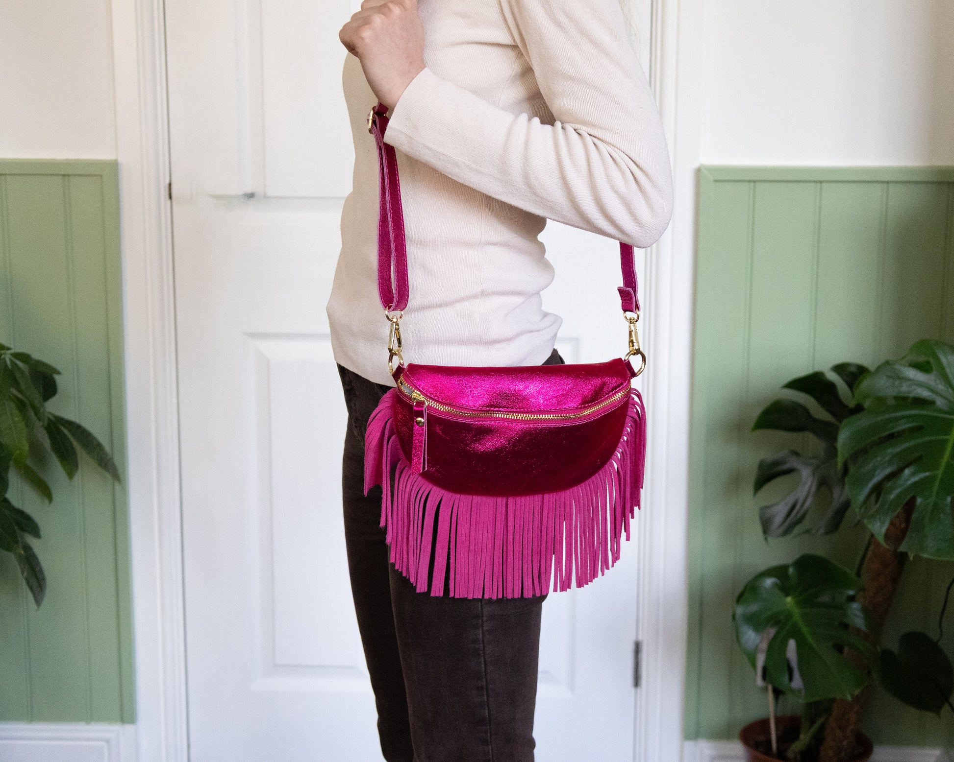 A person wearing a white top is holding a raspberry metallic leather half moon fringed bag with a pink fringe and gold hardware.