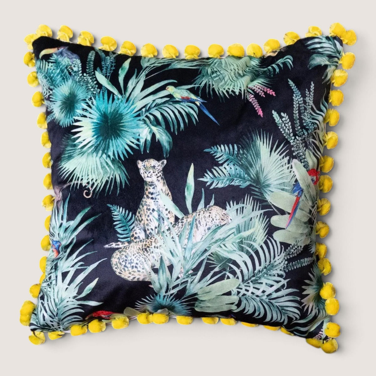 Deepest Jungle velvet cushion with acid yellow pompoms, studio front view showing the black velvet jungle print with a leopard, parrots and palm leaves, handmade in Dorset by Apricot Moon