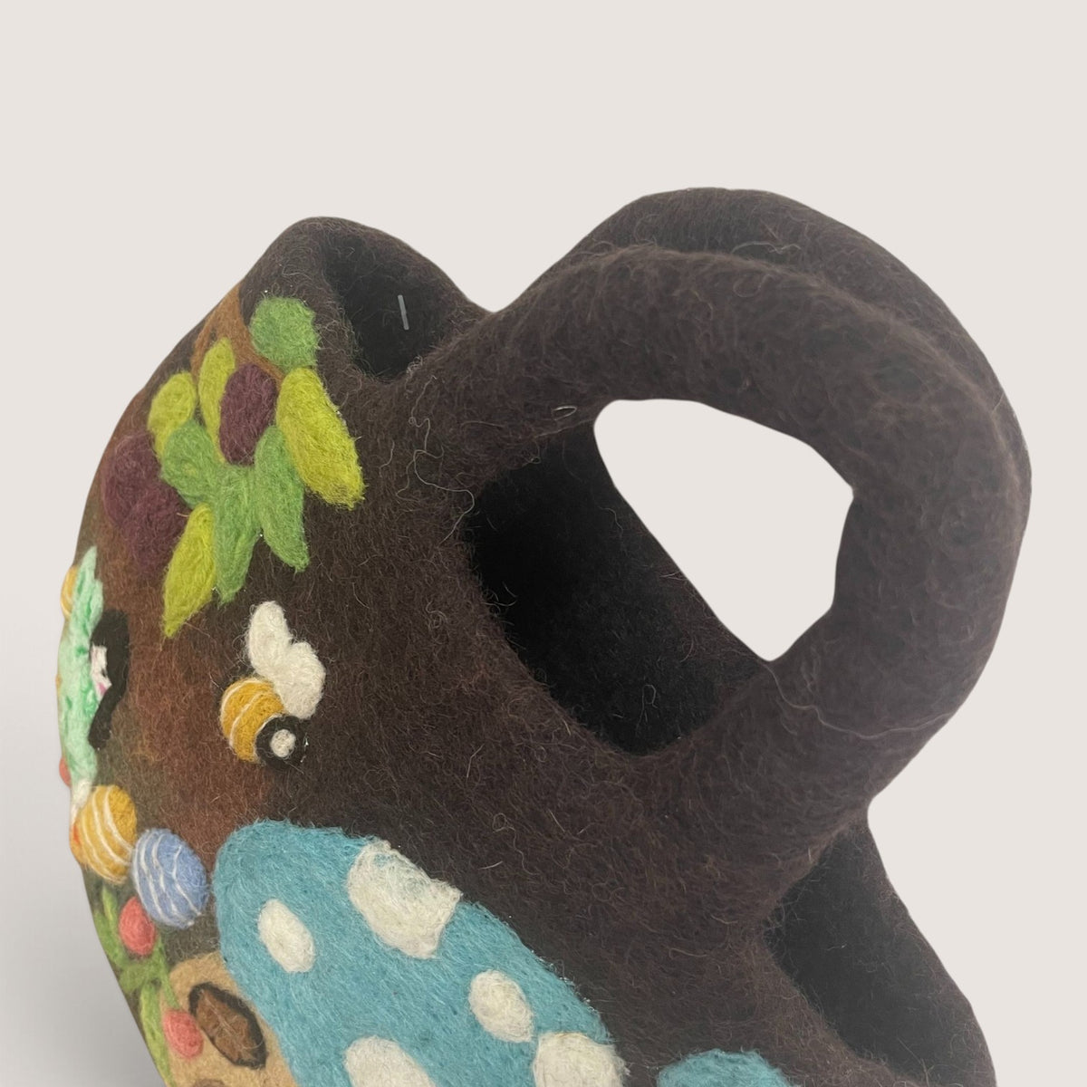 Side view of the Fairy Garden Felted Bag showing the rounded shape, thick felted handle and bee and plum details