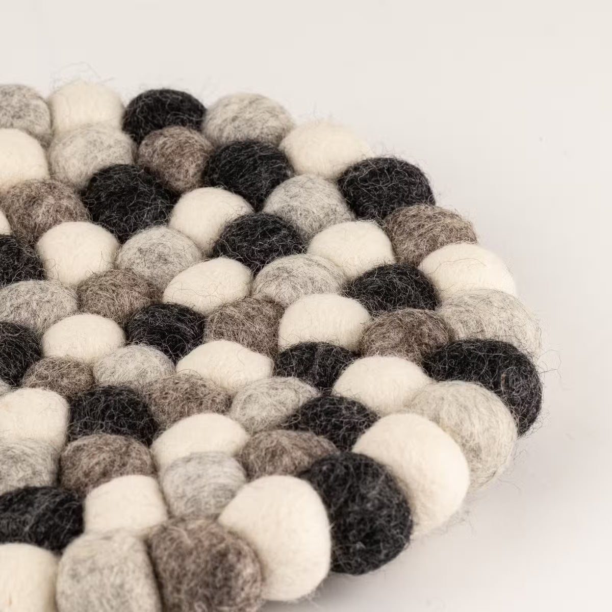 Close-up of the edge of the grey felt ball round placemat, showing charcoal, grey, taupe and cream wool balls