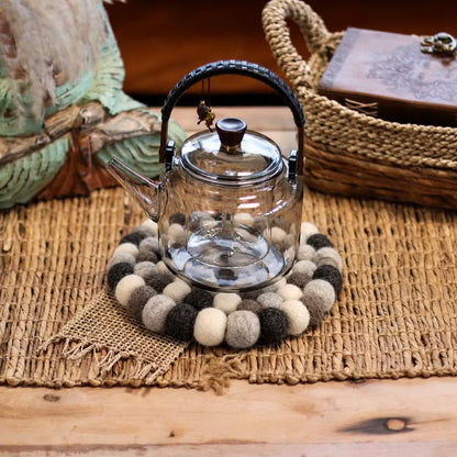 Grey felt ball round placemat under a glass teapot on a woven natural mat
