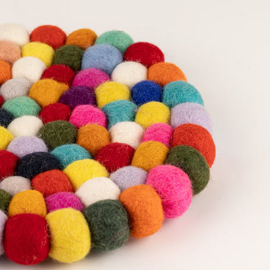 Close-up of the edge of the multicolour felt ball round placemat, showing pink, yellow, blue, orange and green wool balls