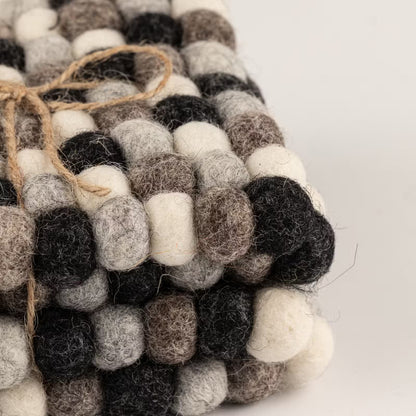 Close-up of stacked grey felt ball coasters tied with jute twine, showing charcoal, grey, taupe and cream wool balls