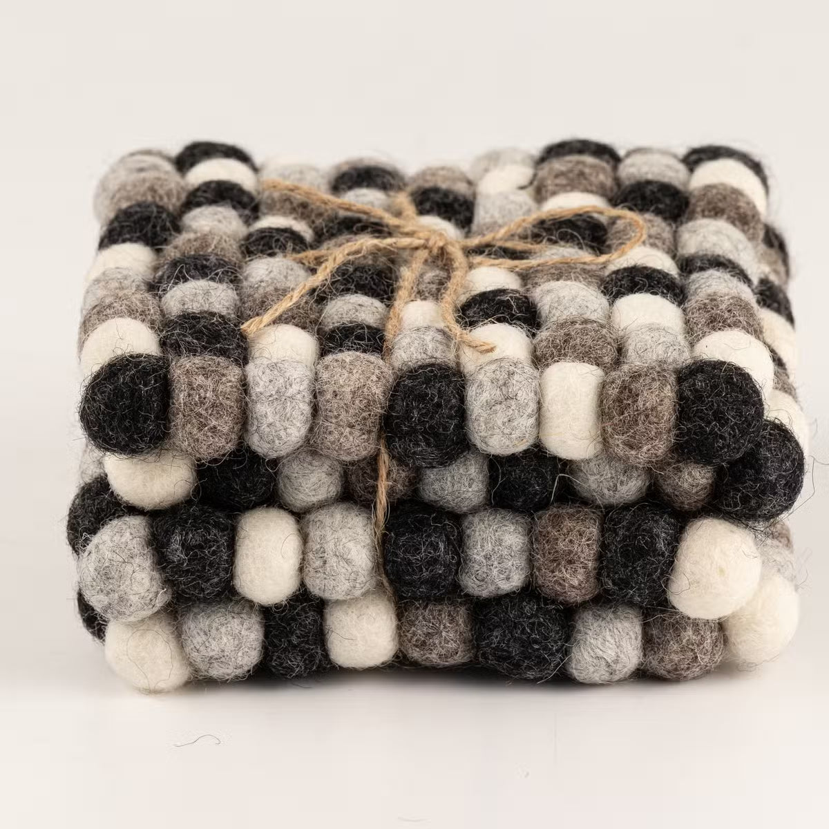 Side view of four grey felt ball square coasters stacked and tied with jute twine