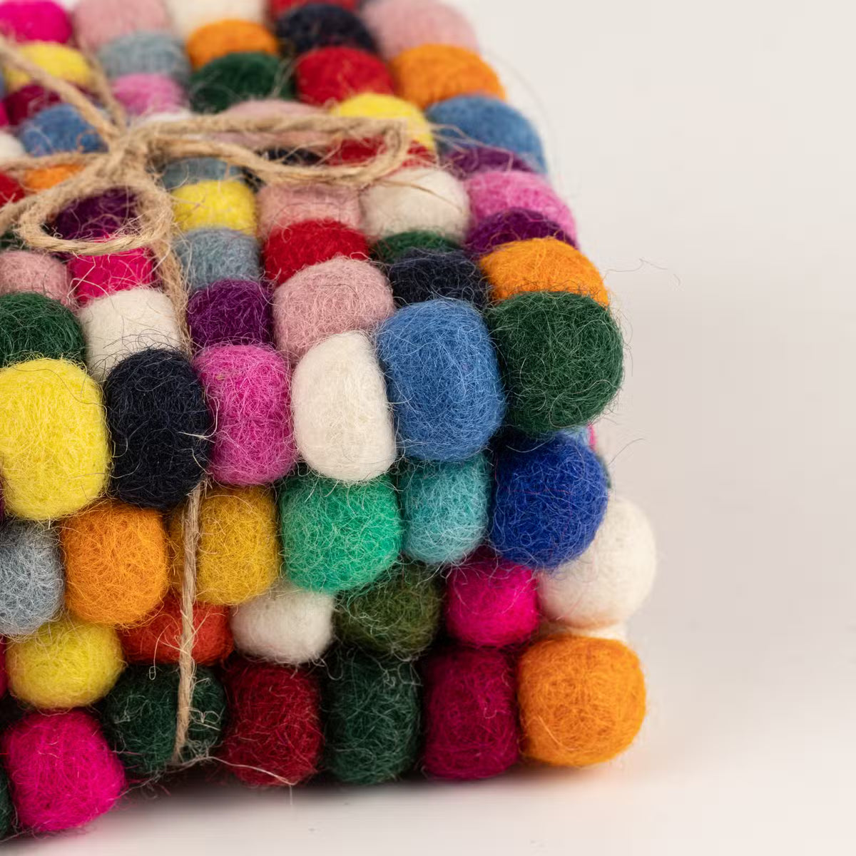Close-up of stacked multicolour felt ball coasters tied with jute twine, showing pink, yellow, blue, green and orange wool balls