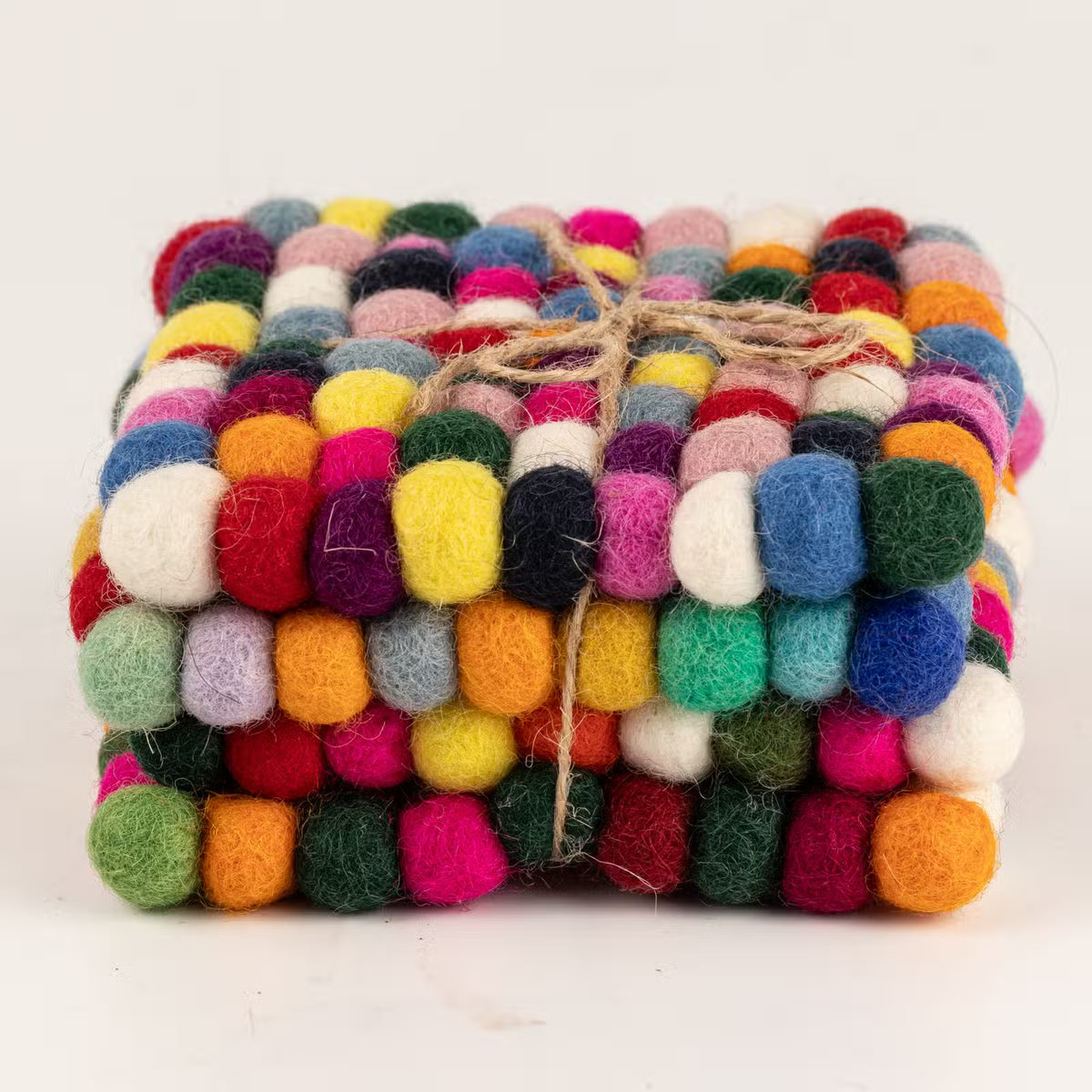 Side view of four multicolour felt ball square coasters stacked and tied with jute twine