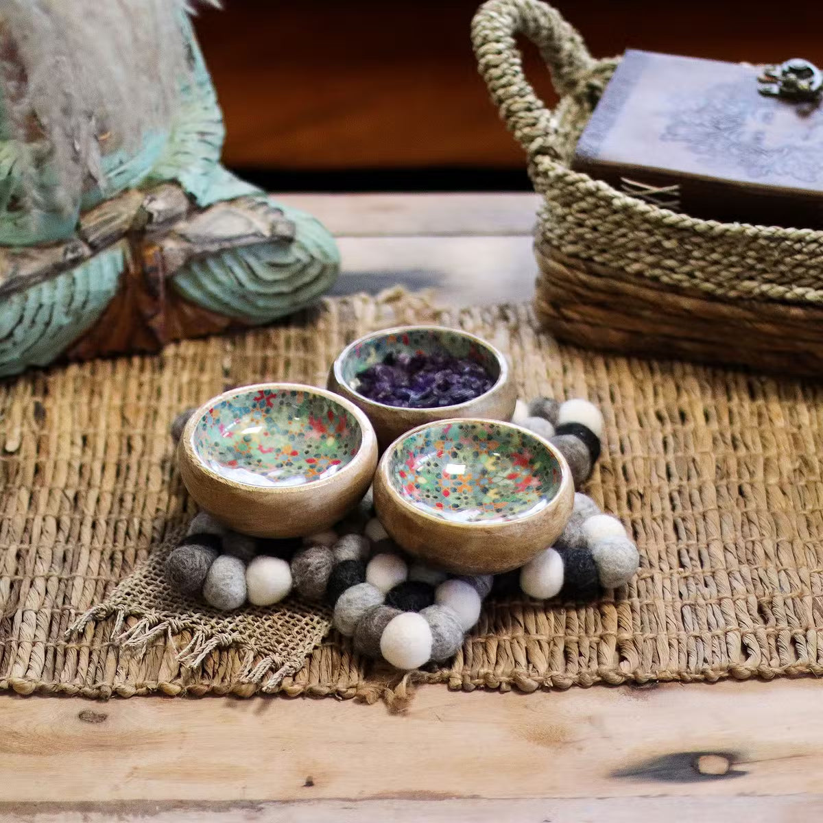Grey felt ball star mat under three small wooden bowls on a woven natural mat