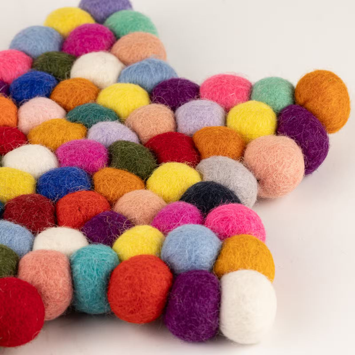 Close-up of one point of the multicolour felt ball star mat, showing pink, orange, yellow, blue and purple wool balls