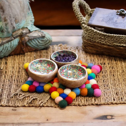 Multicolour felt ball star mat under three small wooden bowls on a woven natural mat