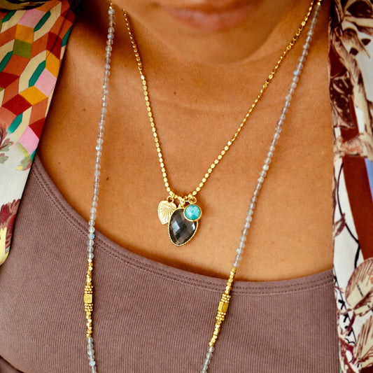 Close-up of a person wearing a gold necklace with a heart-shaped pendant and a colorful scarf.