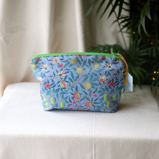 Garden Fruits everyday pouch with a bright green zip on a cream cloth in front of a palm plant