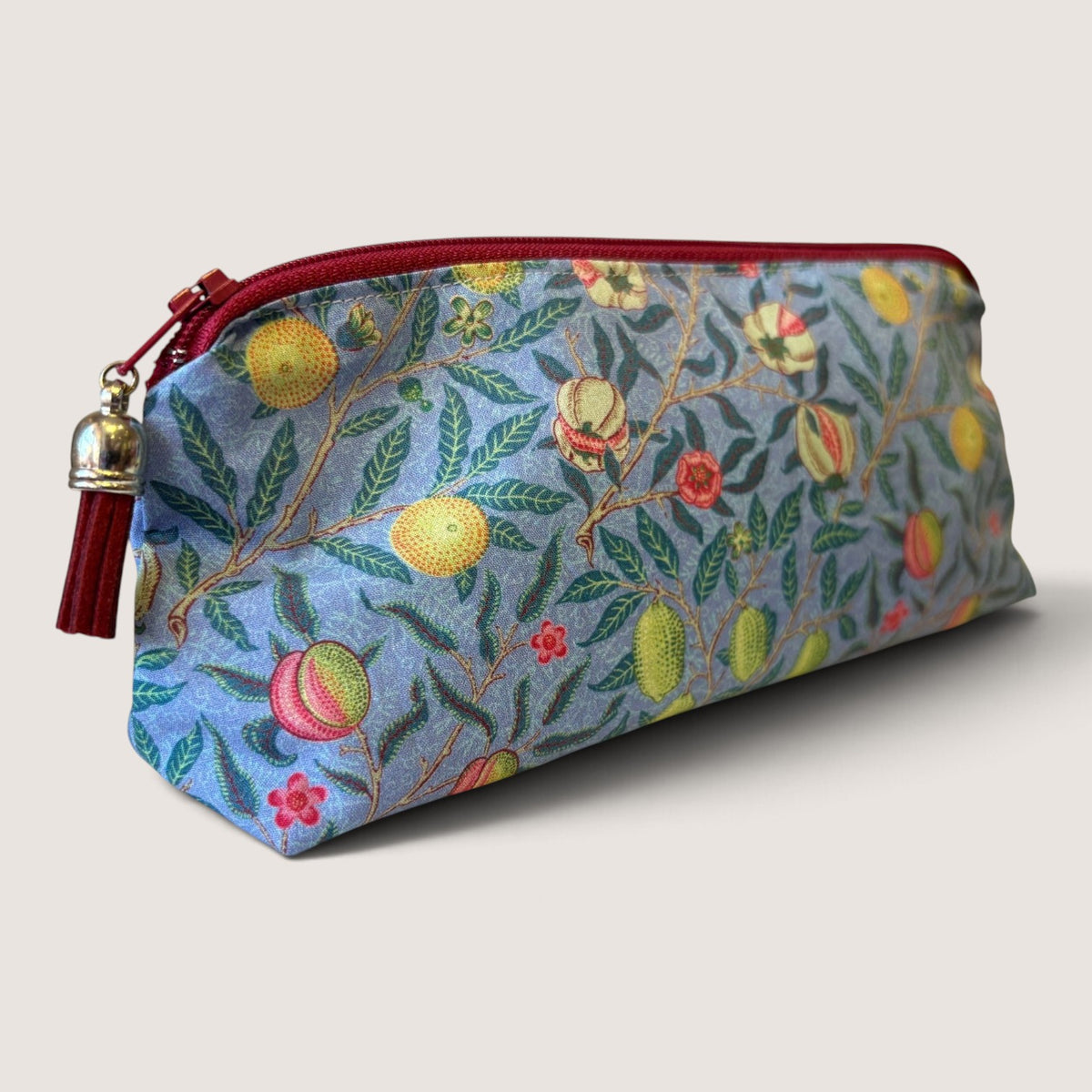 Garden Fruits pencil case in a William Morris fruit print on blue, with a red zip and tassel, angled view