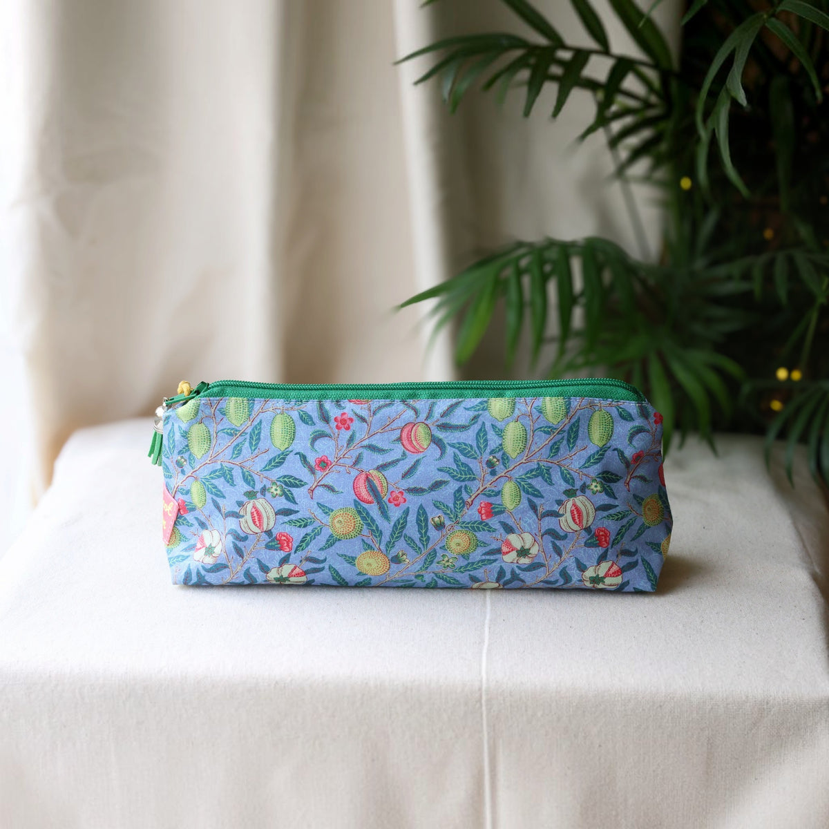 Garden Fruits pencil case with a green zip standing on a cream cloth beside a green palm plant