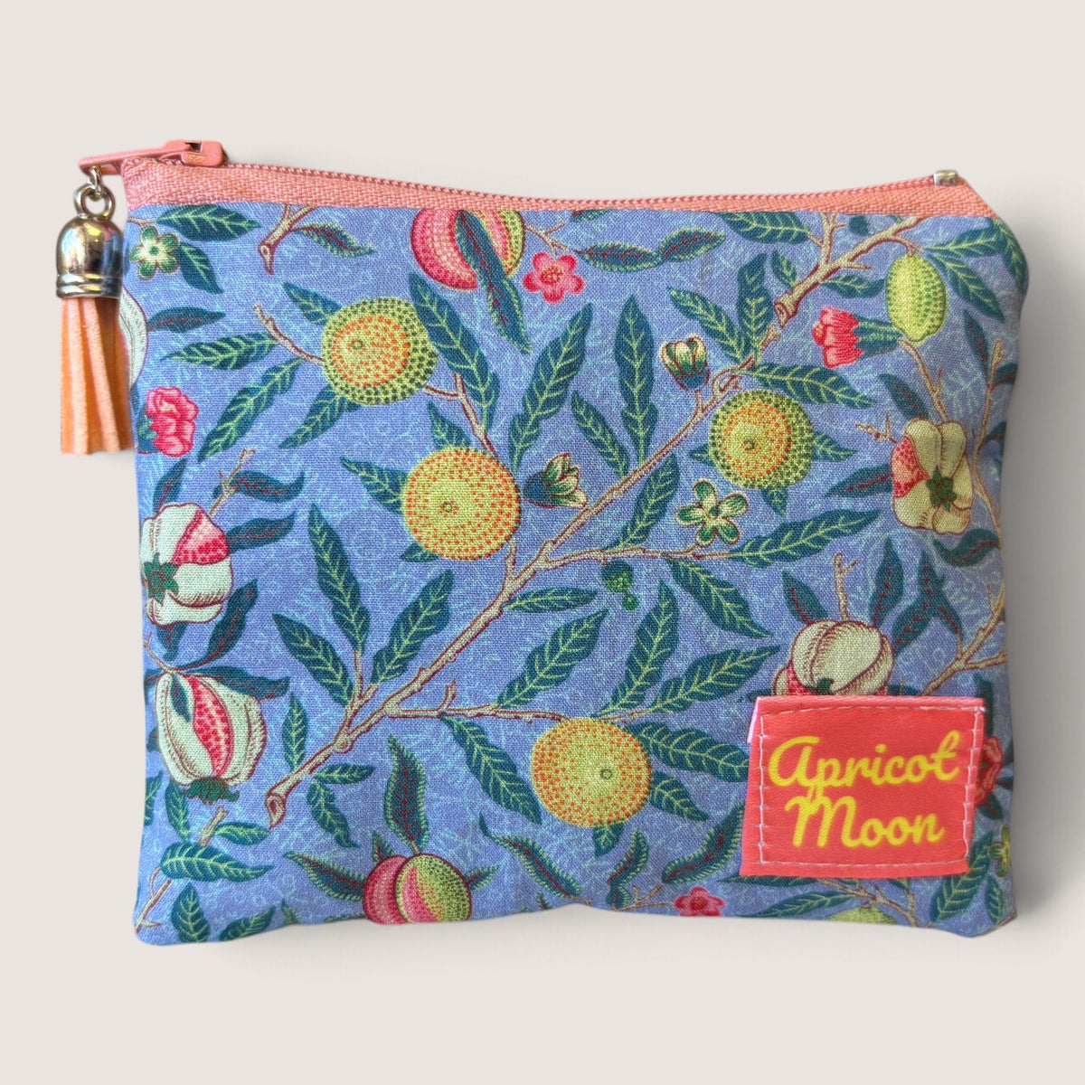 Garden Fruits purse with a pale blue zip standing on a cream cloth beside a green palm plant