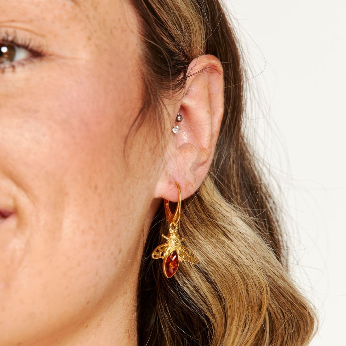 Close-up of a woman's ear wearing a gold bee-shaped earring with a red gemstone.