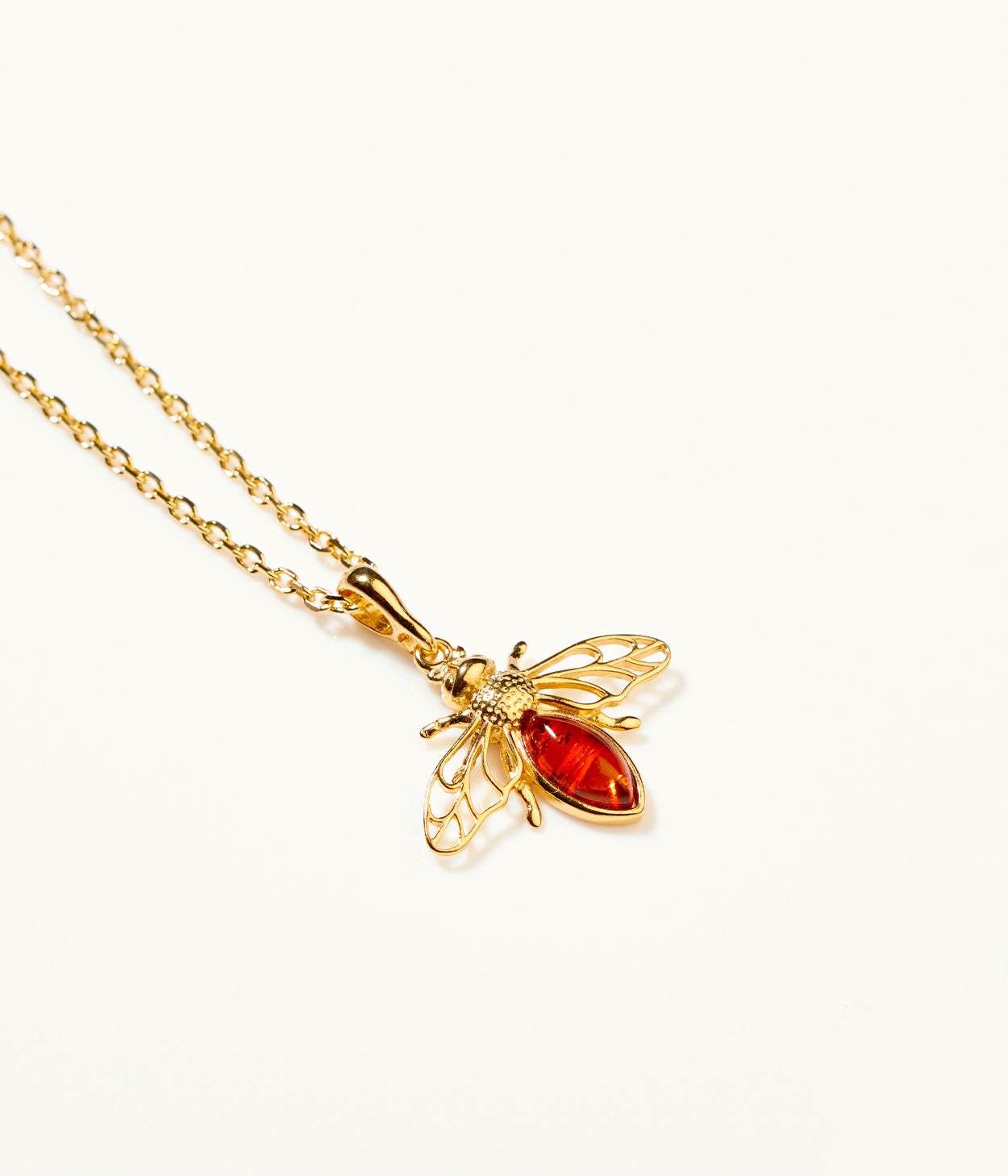 Gold necklace with a bee pendant featuring a red gemstone on a white background