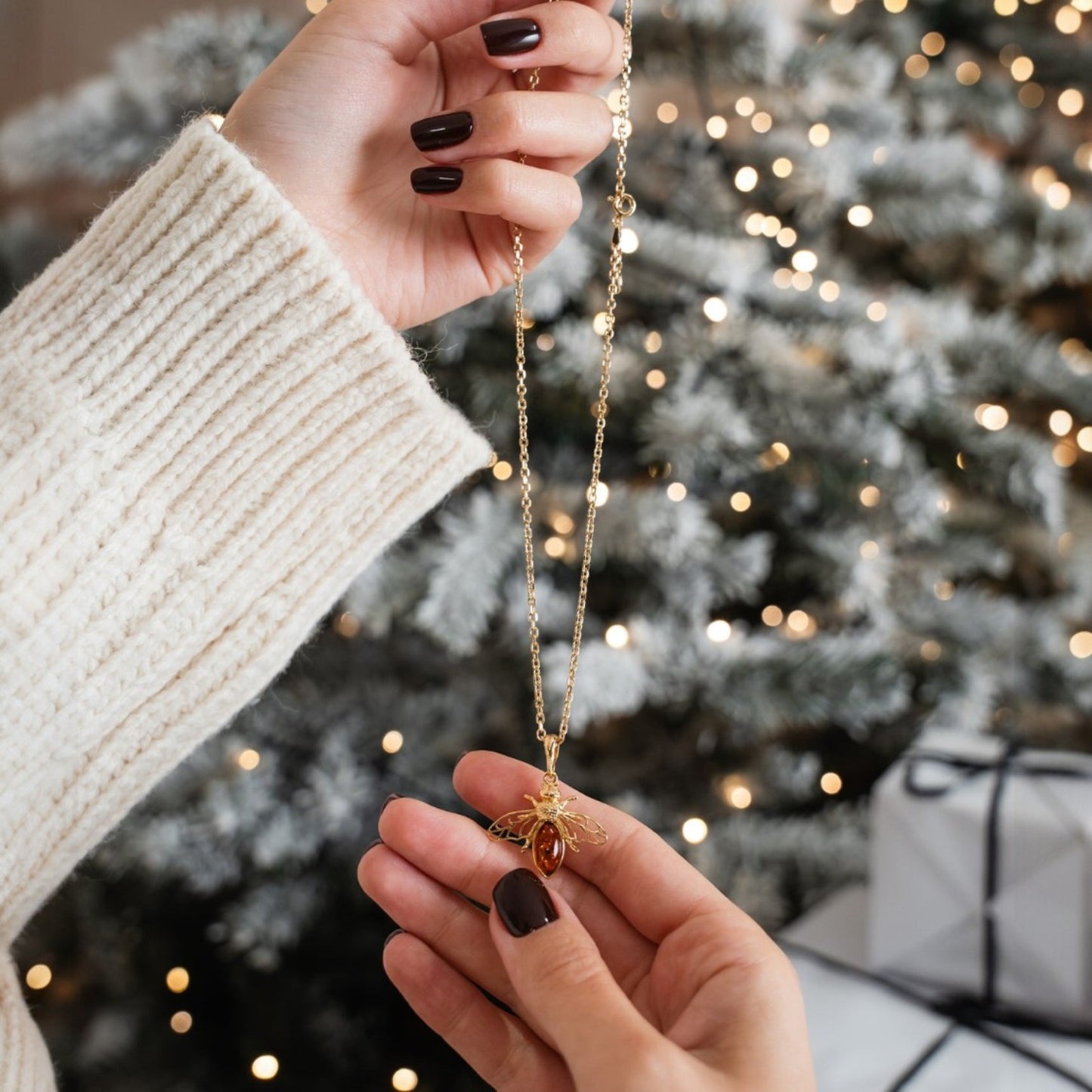 Person holding a gold necklace with a Christmas tree and gift in the background
