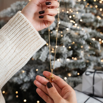Person holding a gold necklace with a Christmas tree and gift in the background