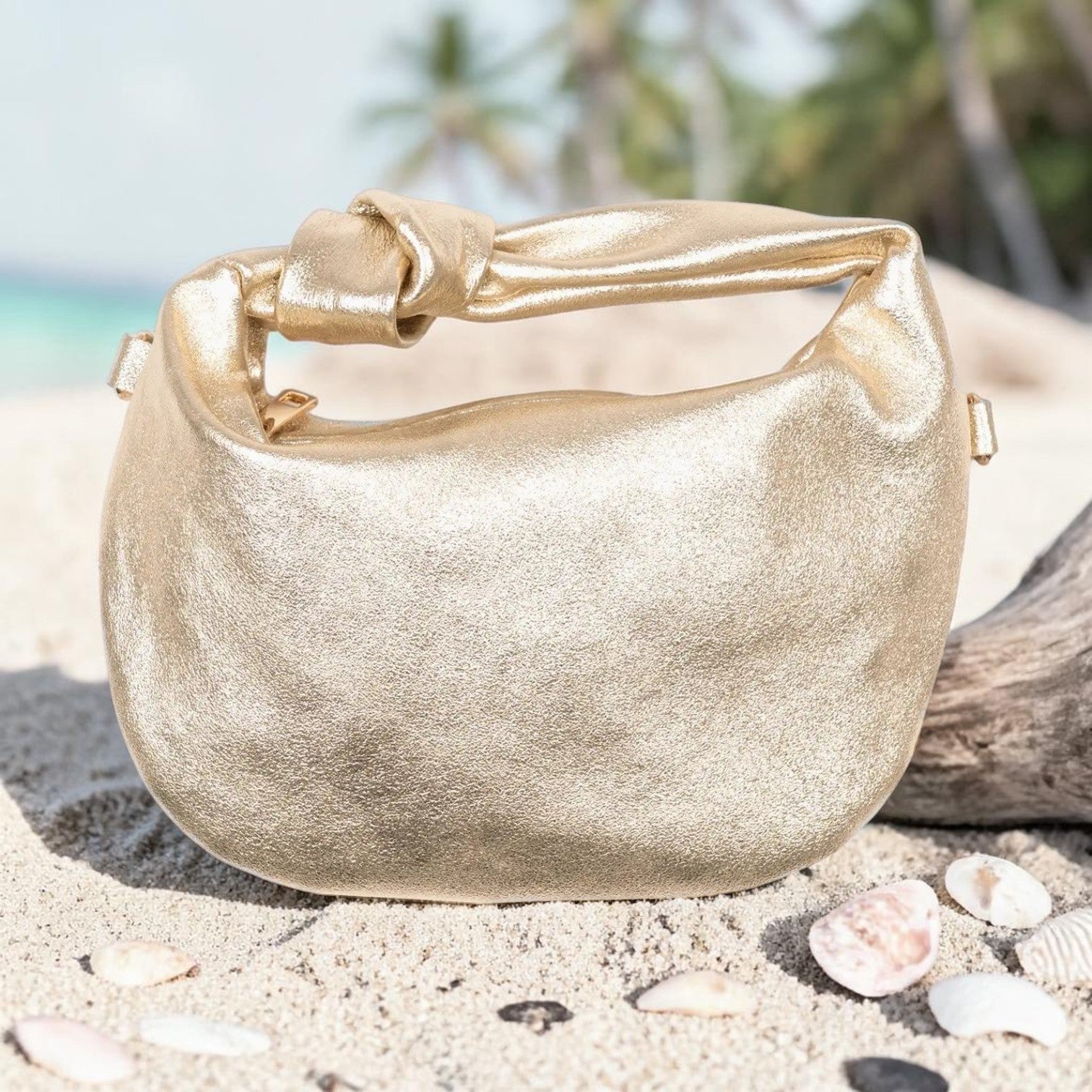 Gold handbag on a sandy beach with shells and driftwood