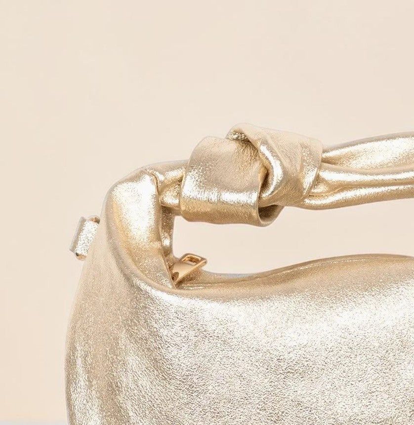 Close-up of a gold metallic handbag with a buckle on a beige background