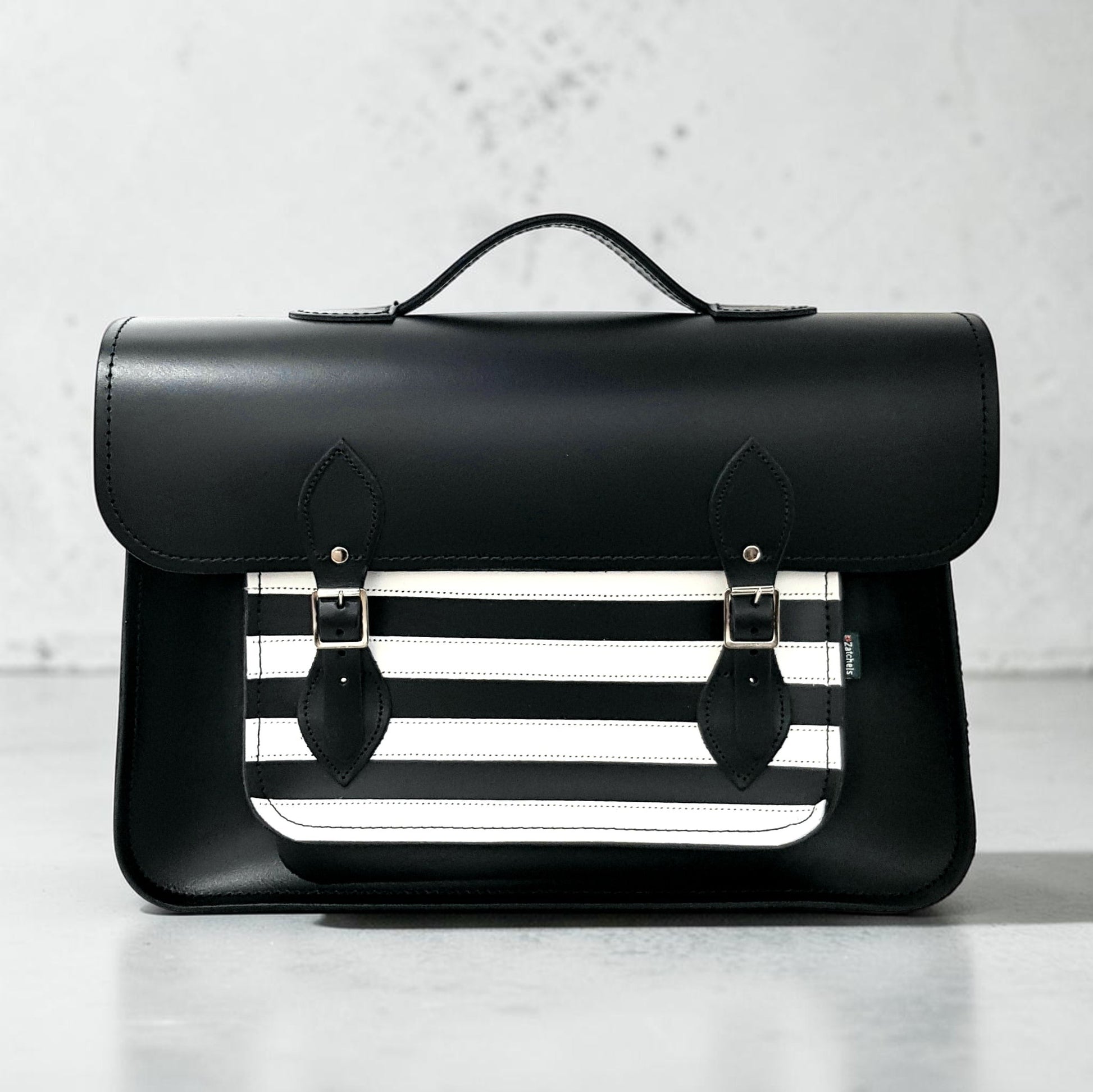 Black leather satchel with a white stripe design on a light gray background