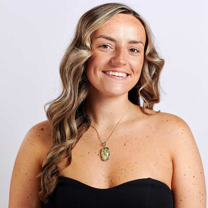 Woman with long wavy hair wearing a black top and a necklace with a pendant on a light purple background