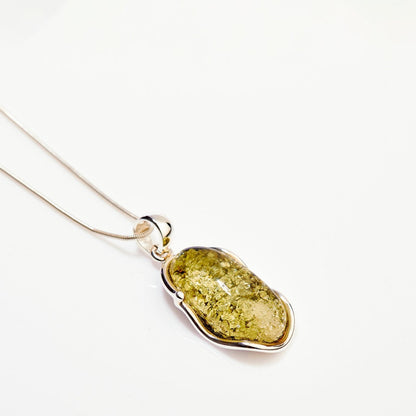 Green amber pendant on a silver chain against a white background