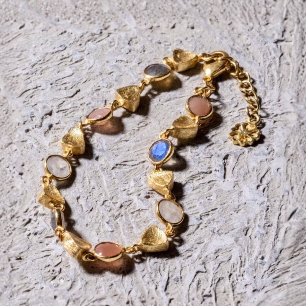 Gold bracelet with colorful stones on a textured gray surface
