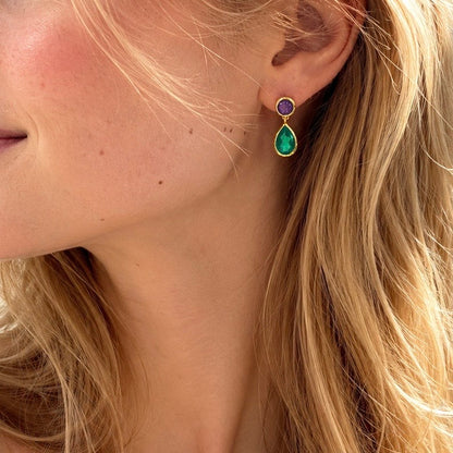 Close-up of a person wearing a gold earring with a purple and green gemstone.