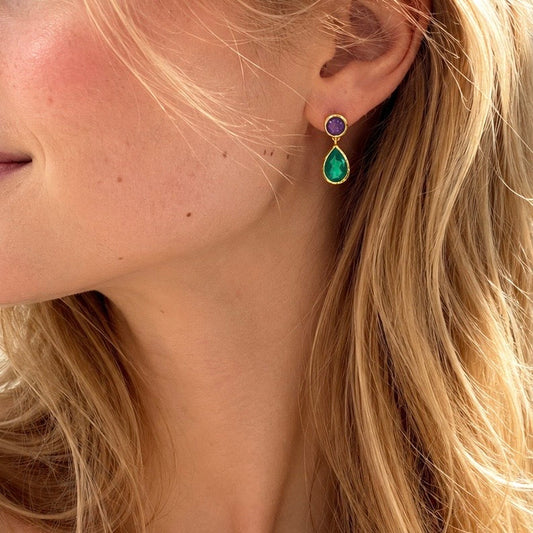 Close-up of a person wearing a gold earring with a purple and green gemstone.