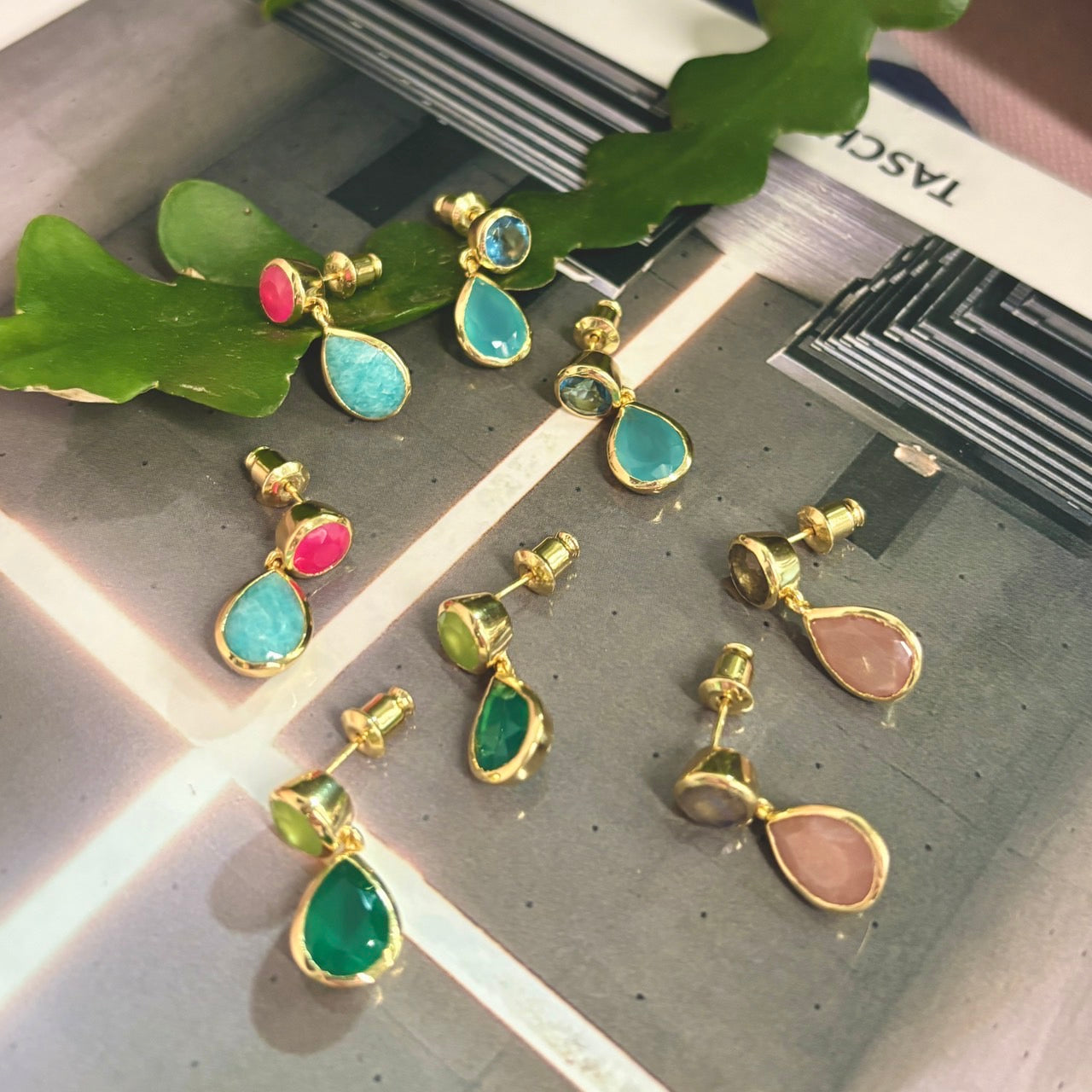 Colorful teardrop-shaped earrings on a textured surface with green leaves.